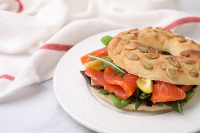 Tasty bagel with salmon and tomatoes on white marble table, closeup. Space for text