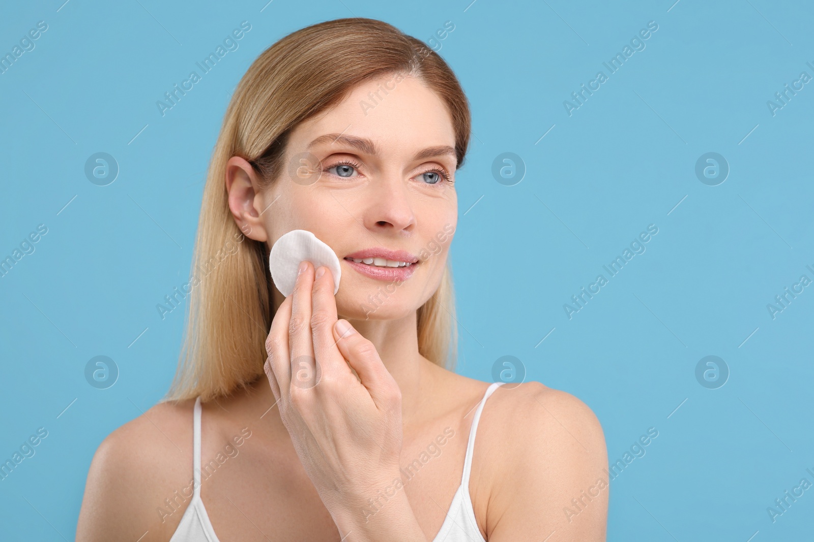 Photo of Beautiful woman removing makeup with cotton pad on light blue background