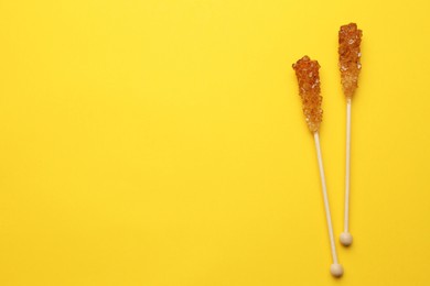 Photo of Wooden sticks with sugar crystals and space for text on yellow background, flat lay. Tasty rock candies