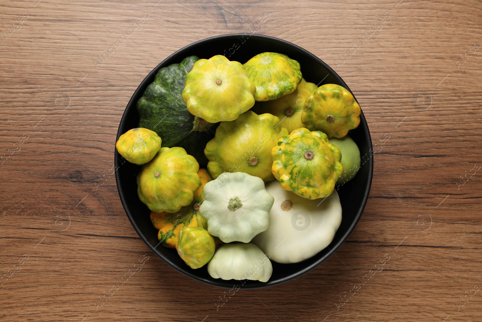 Photo of Fresh ripe pattypan squashes in bowl on wooden table, top view