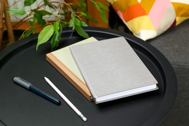 Books, pen and pencil on black table near sofa indoors, closeup