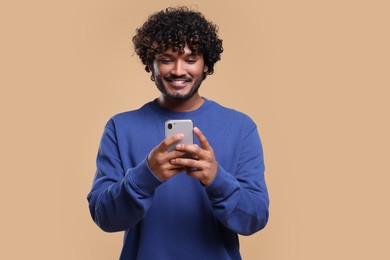 Photo of Handsome smiling man using smartphone on beige background