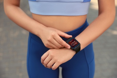 Image of Woman using stylish smart watch during training outdoors, closeup