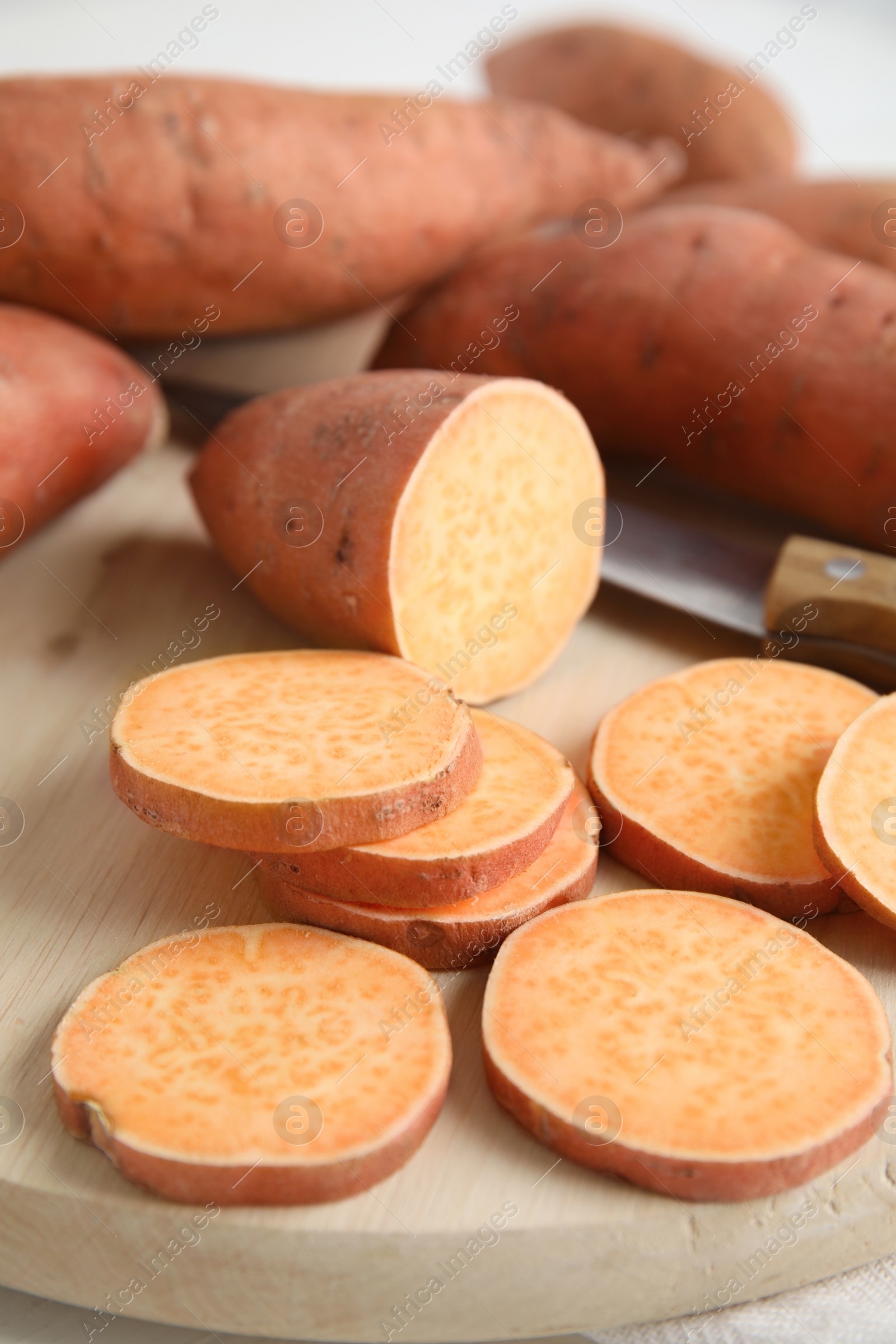 Photo of Whole and cut ripe sweet potatoes on wooden board, closeup