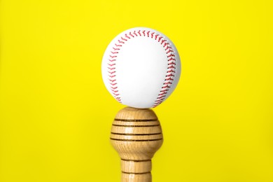 Photo of White ball on wooden baseball bat against yellow background, closeup. Sports equipment