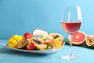 Delicious exotic fruits and glass of wine on light blue wooden table