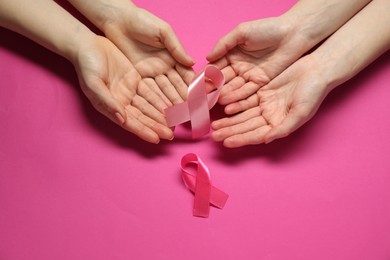 Women with pink ribbons on color background, top view. Breast cancer awareness