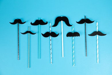 Photo of Fake paper mustaches with party props on light blue background, flat lay