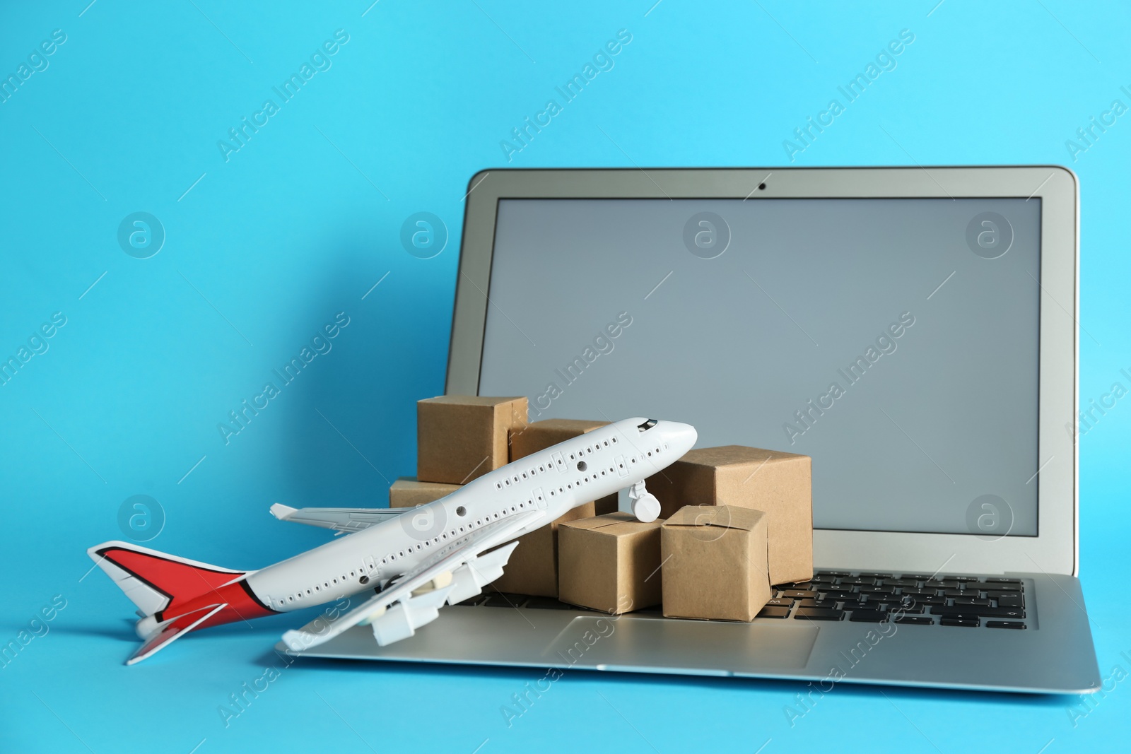 Photo of Laptop, airplane model and carton boxes on light blue background. Courier service