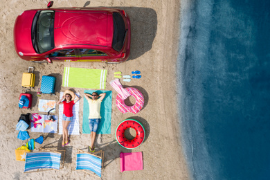 Couple with beach accessories and car near river, aerial view. Summer trip