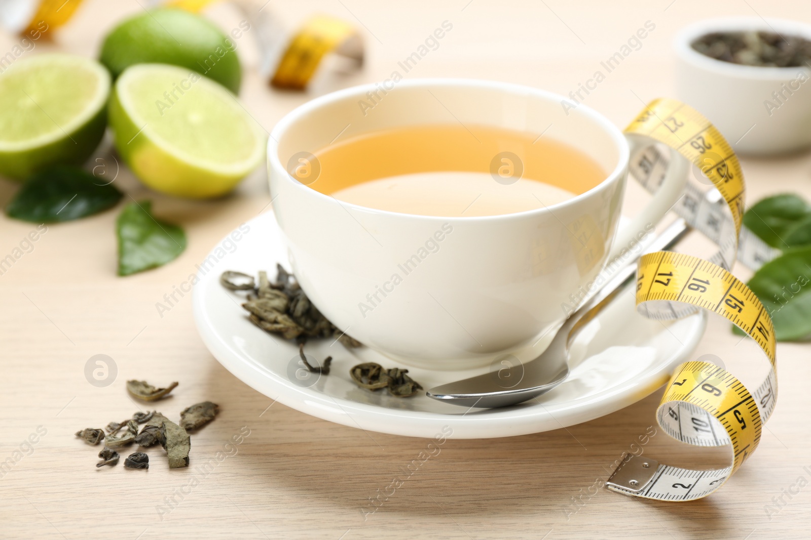 Photo of Cup of diet herbal tea, measuring tape and dried leaves on wooden table