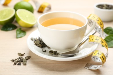 Photo of Cup of diet herbal tea, measuring tape and dried leaves on wooden table