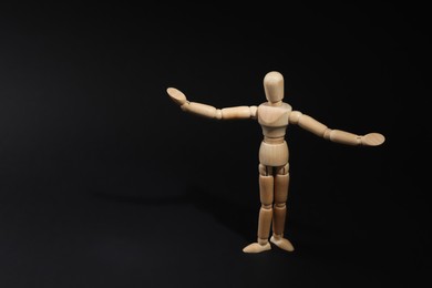 Photo of Wooden human model on black background, space for text. Mini mannequin