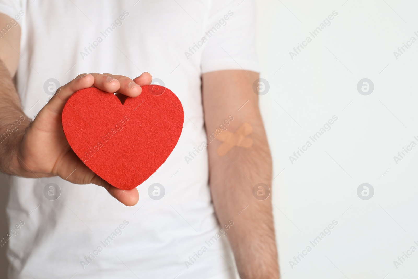 Photo of Man holding fabric heart near hand with adhesive plasters against white background, closeup. Blood donation concept