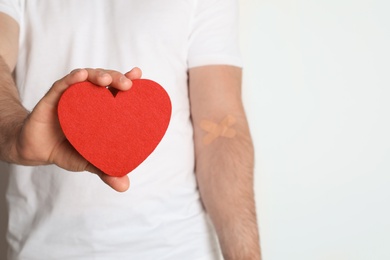 Man holding fabric heart near hand with adhesive plasters against white background, closeup. Blood donation concept