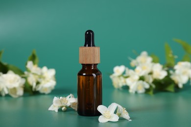 Photo of Essential oil in bottle and beautiful jasmine flowers on green background