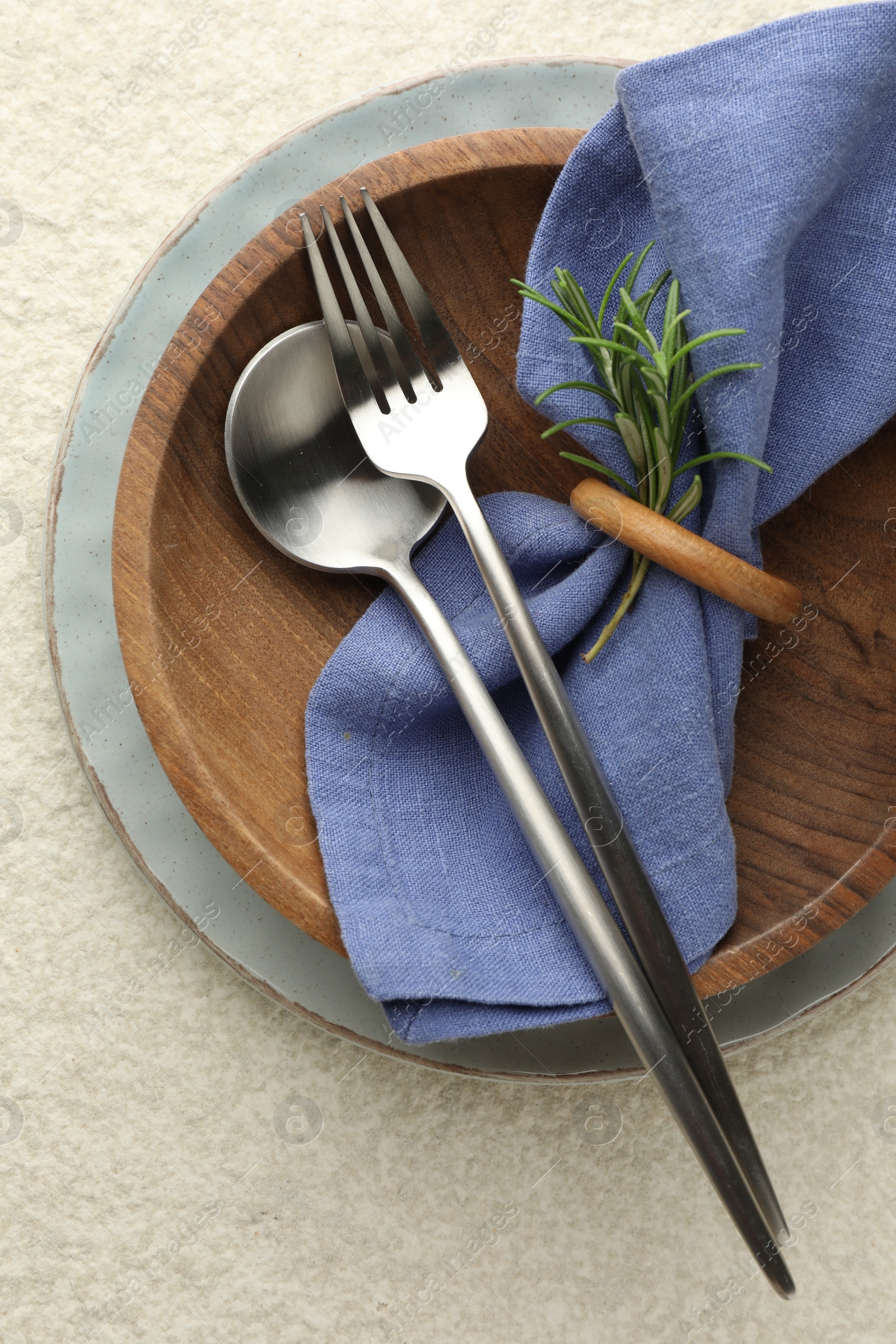 Photo of Stylish setting with cutlery, napkin, rosemary and plates on light textured table, top view