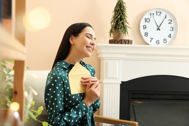 Photo of Happy woman holding Christmas greeting card in living room