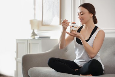 Woman eating tasty granola with fresh berries and yogurt on sofa at home