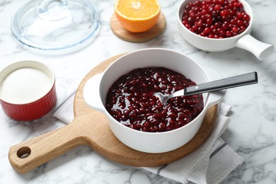 Photo of Fresh cranberry sauce in bowl served on white marble table, closeup