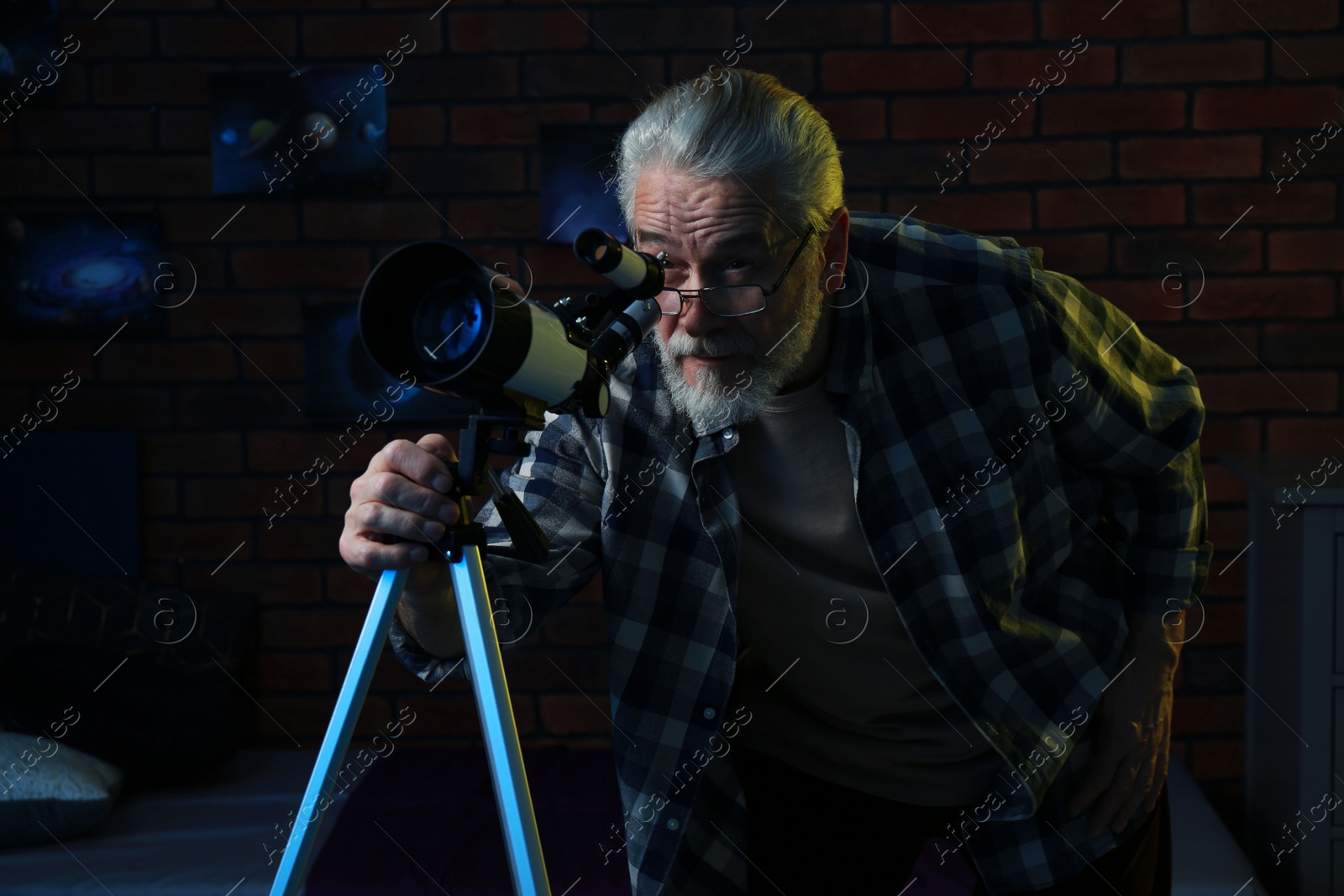 Photo of Senior man looking at stars through telescope in room