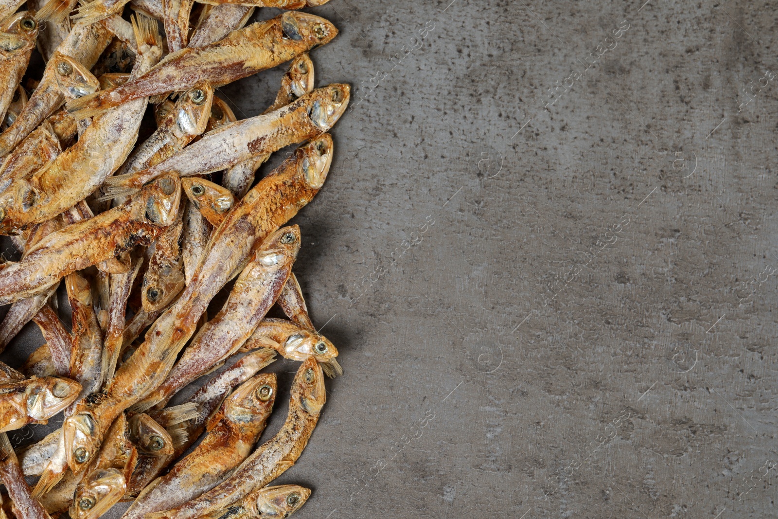 Photo of Tasty dried anchovies on grey table, flat lay. Space for text