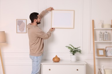 Photo of Man hanging picture frame on white wall at home