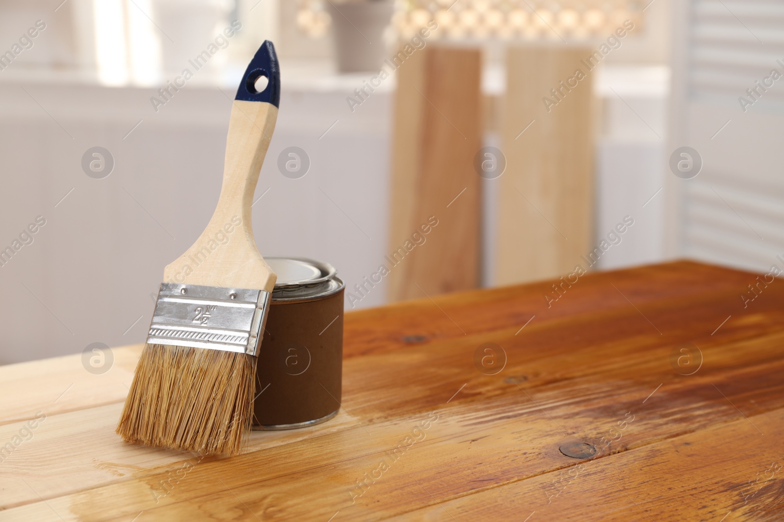 Photo of Brush and can with wood stain on wooden surface indoors, space for text