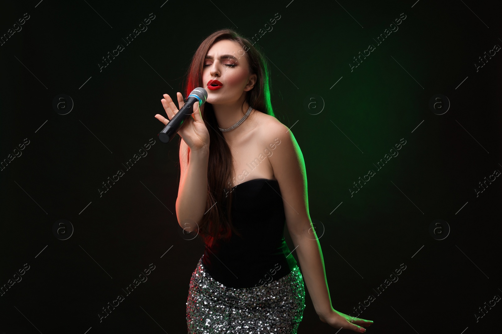 Photo of Beautiful woman with microphone singing in color lights on dark background