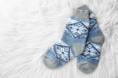 Photo of Knitted socks on white faux fur, flat lay. Space for text