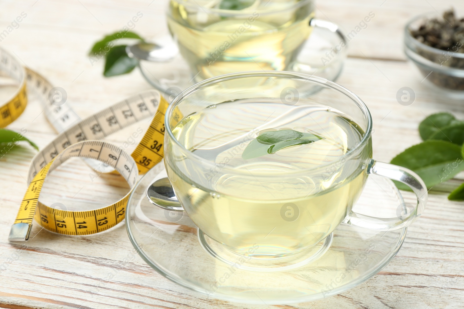 Photo of Diet herbal tea with green leaf and measuring tape on white wooden table