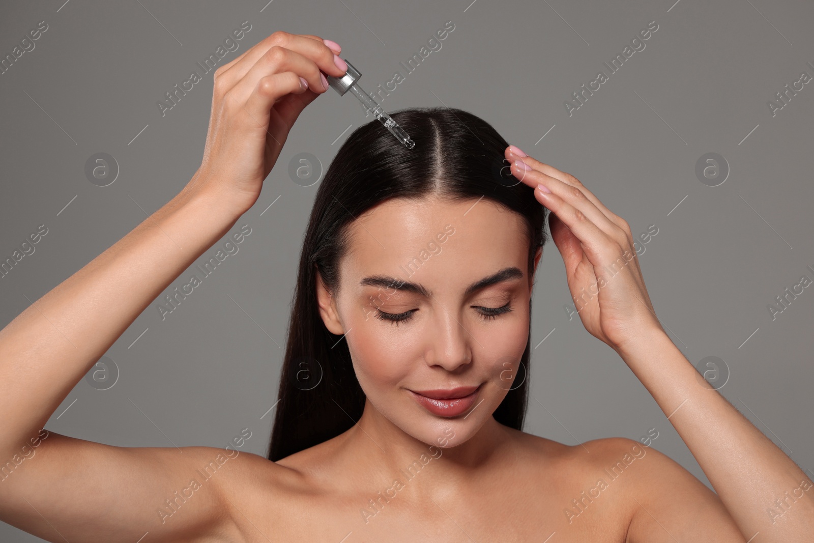 Photo of Beautiful woman applying hair serum on grey background. Cosmetic product