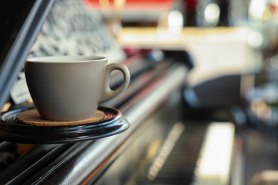 Photo of Cup with cork coaster on grand piano in cafe, closeup. Space for text