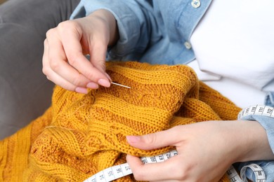 Photo of Woman sewing sweater with needle, closeup view