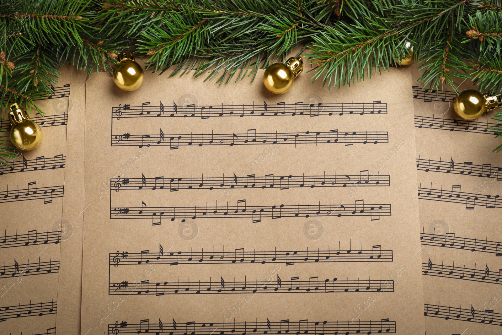 Photo of Fir branches and golden balls on Christmas music sheets, above view