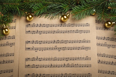 Fir branches and golden balls on Christmas music sheets, above view