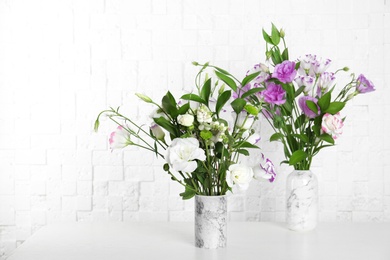 Photo of Vases with beautiful flowers on table near brick wall