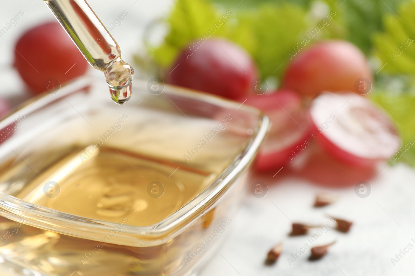 Photo of Dripping natural grape seed oil into bowl on table, closeup. Organic cosmetic