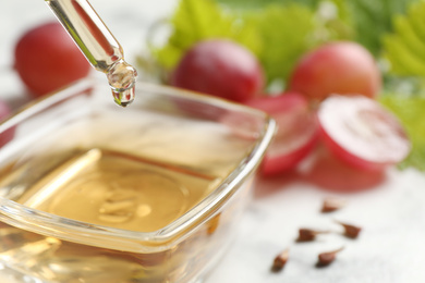 Photo of Dripping natural grape seed oil into bowl on table, closeup. Organic cosmetic