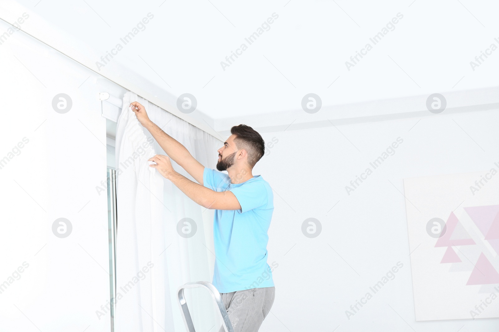 Photo of Young handsome man hanging window curtain in room