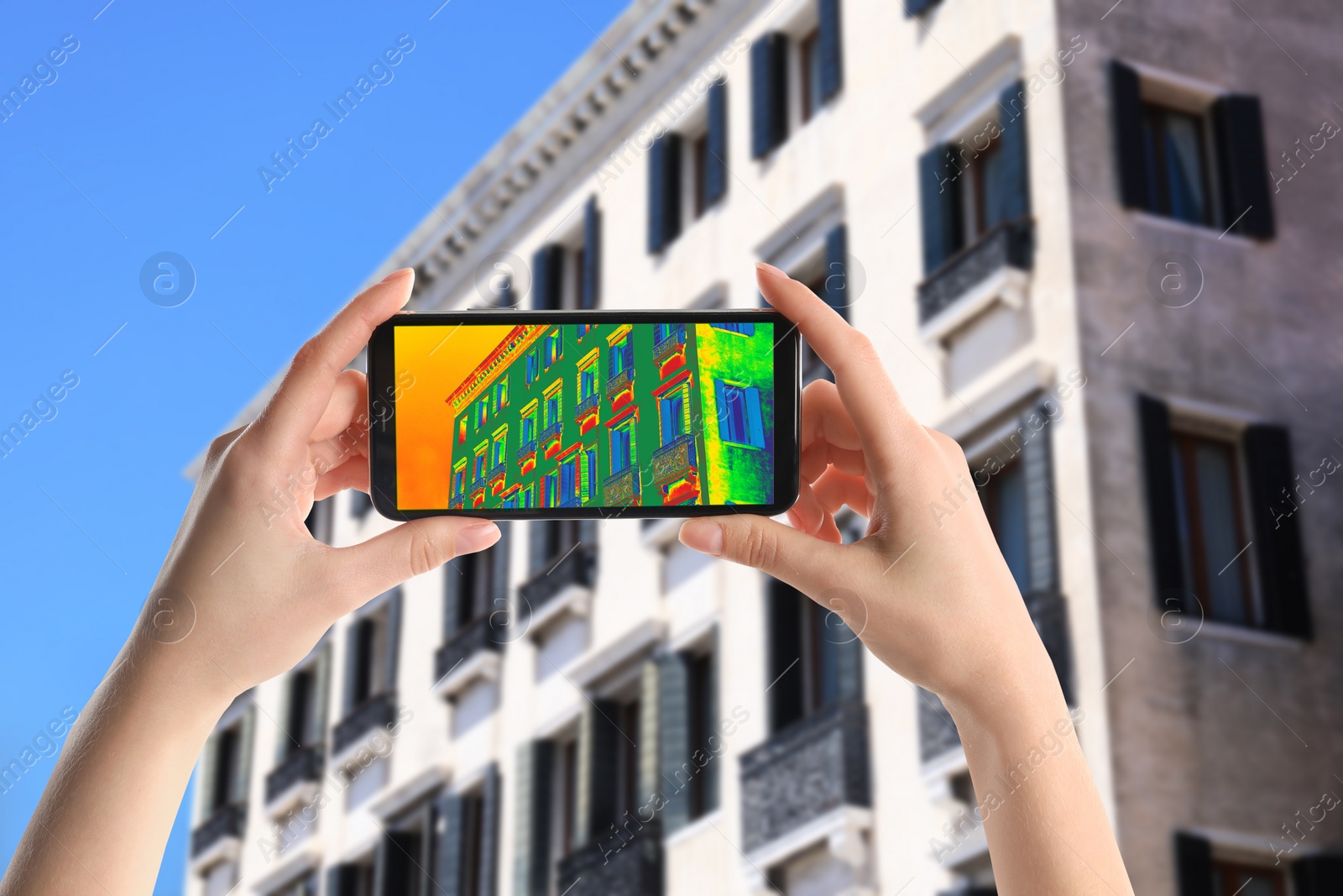 Image of Woman detecting heat loss in building using thermal viewer on smartphone, outdoors. Energy efficiency