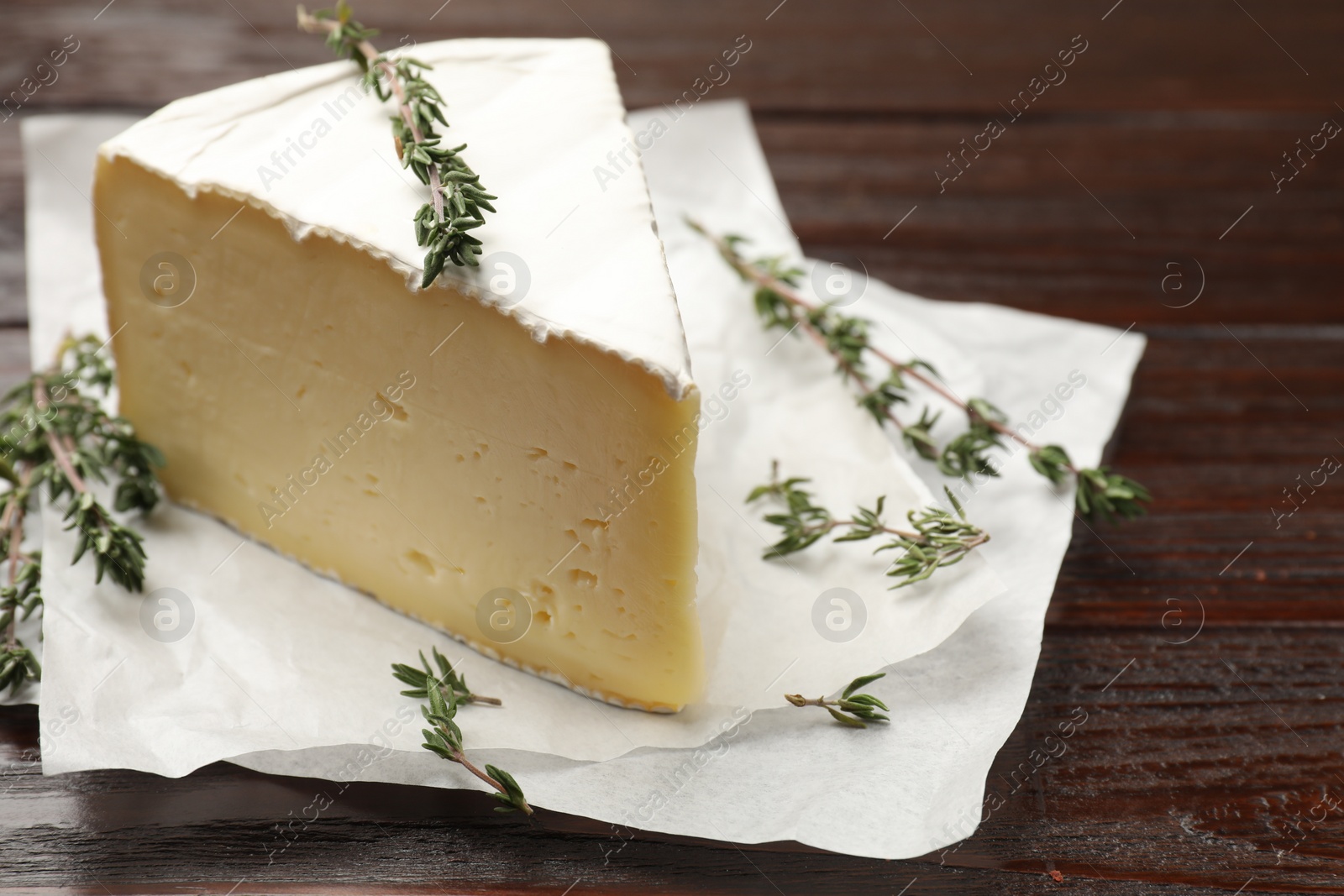 Photo of Piece of tasty camembert cheese and thyme on wooden table, closeup