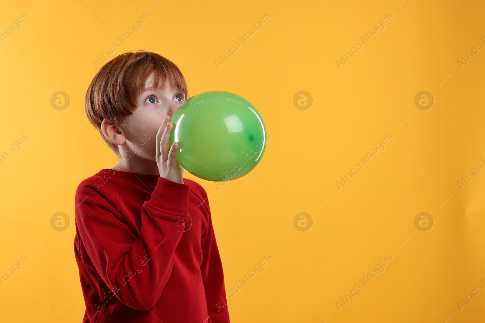 Photo of Boy inflating green balloon on orange background, space for text