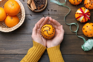 Photo of Woman holding pomander ball made of tangerine with cloves at wooden table, top view