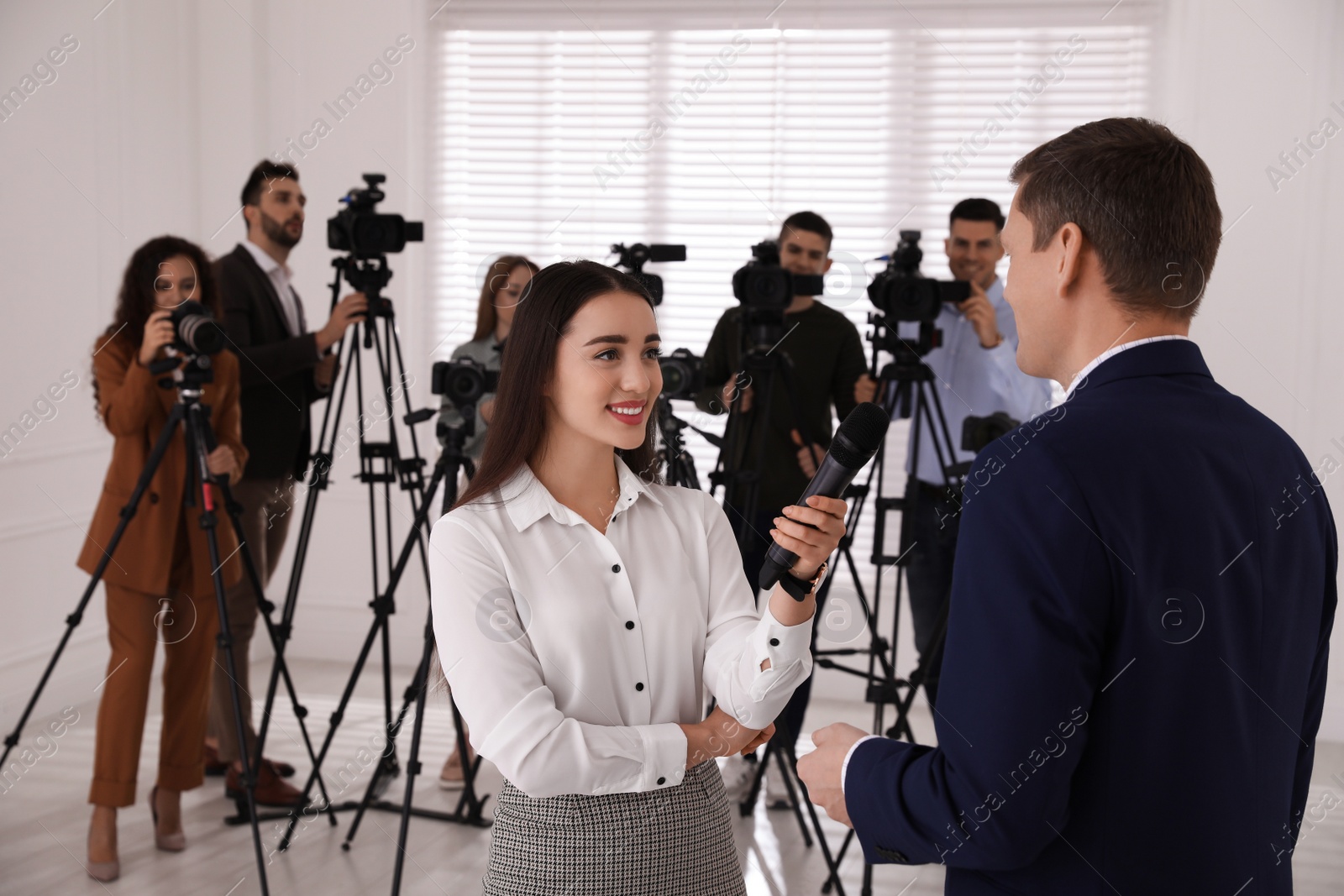 Photo of Professional young journalist interviewing businessman and group of video camera operators on background