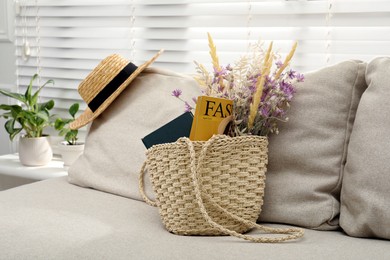 Stylish beach bag with wildflowers, magazine and book on sofa in room