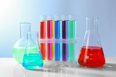 Photo of Different laboratory glassware with colorful liquids on white table against grey background