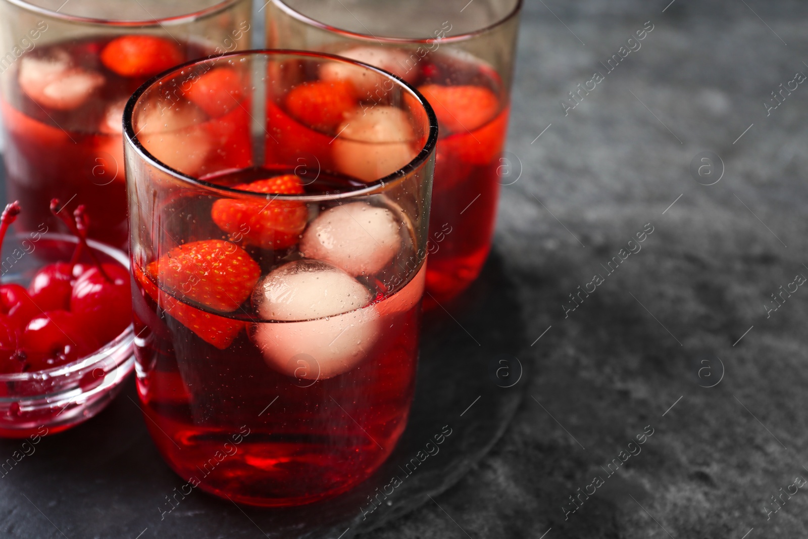 Photo of Delicious strawberry cocktails served with ice balls and cherries on grey table, space for text