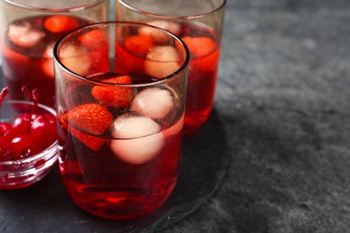 Delicious strawberry cocktails served with ice balls and cherries on grey table, space for text