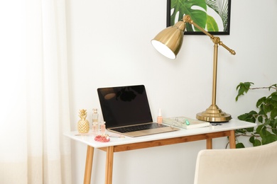 Photo of Stylish workplace with modern laptop and cosmetic products on table near light wall. Beauty blogger